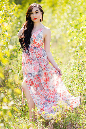 Beautiful brunette model in a beautiful light flower dress walking through a sunlit field