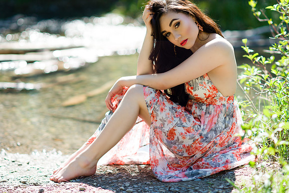 Fashion brunette woman model sitting near a creek in a light and long flower dress in Calgary