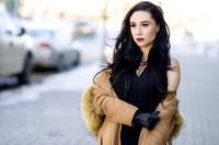 Brunette high fashion woman model removing her winter coat and revealing a black dress without sleeves, on a windy day on the last days of Winter.