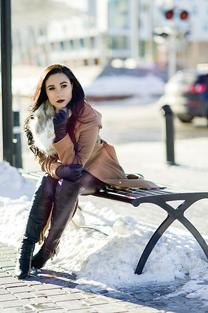Brunette high fashion woman model in a beige winter coat with fur collar  and knee high boots, on a cold winter day in downtown Calgary