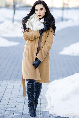 Brunette high fashion woman model in a beige winter coat with fur collar  and knee high boots, on a cold winter day in downtown Calgary