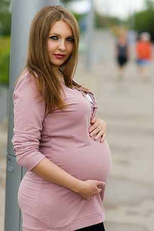 Beautiful pregnant young brunette woman wearing a pink long sleeved shirt in Calgary