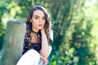 Green eye woman model resting on a wooden fence wearing black choker and black dress