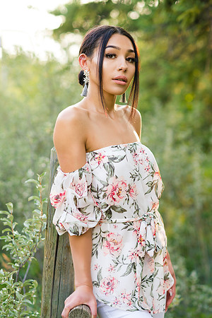 teen woman model with flower top resting on wooden fence in forest